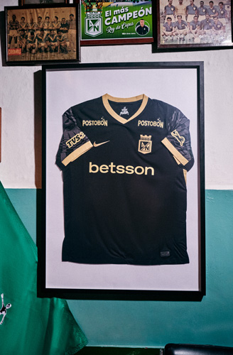 Camiseta negra de visitante de Atlético Nacional 2025 enmarcada sobre un bar decorado con objetos del club.